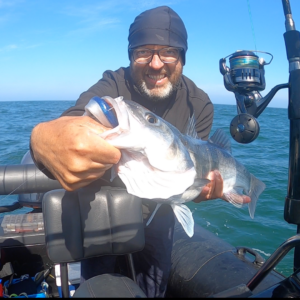 Le guide de pêche se trouve au centre de l'image sur son zodiac, on aperçoit une canne à pêche à gauche de la photo. Il tient le poisson dans ses mains nues sur son bateau en mer aux alentours de Saint-Michel-Chef-Chef.